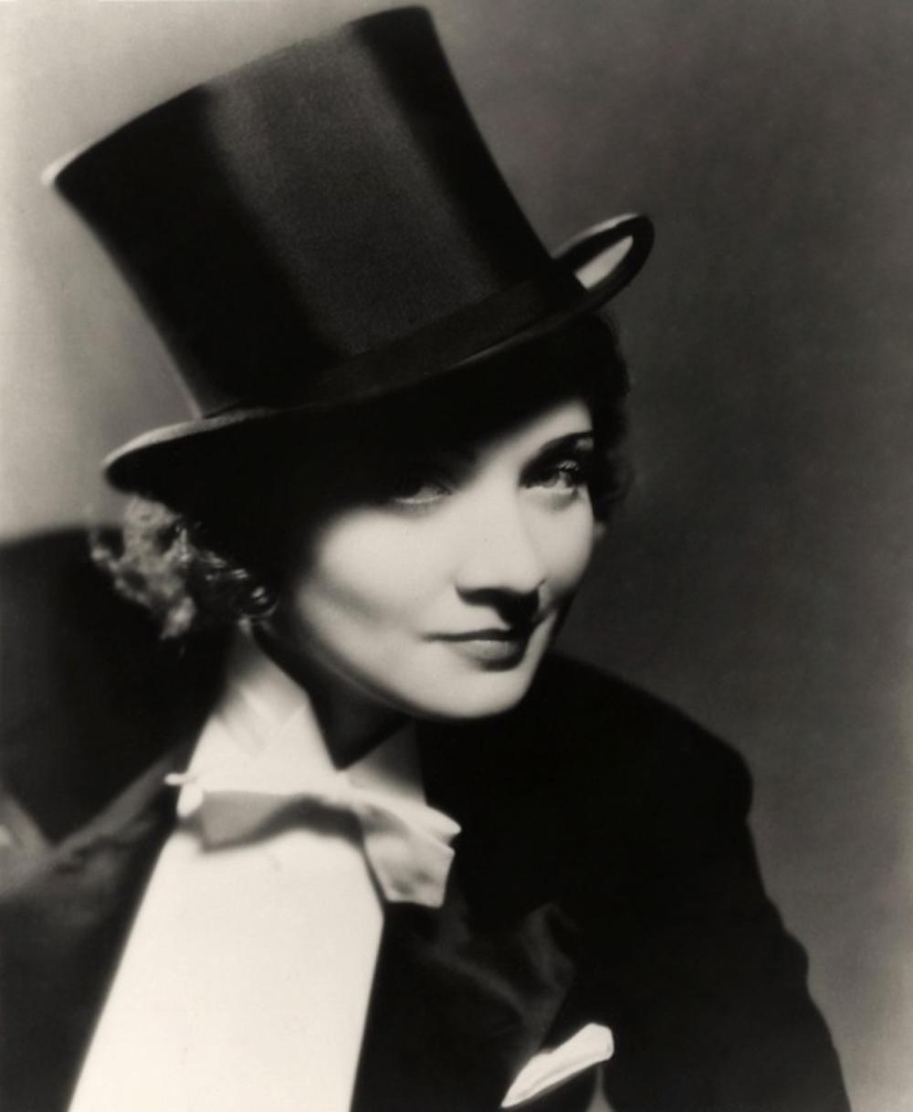 Black and white photo of white woman with curly hair in a top hat and formal tux