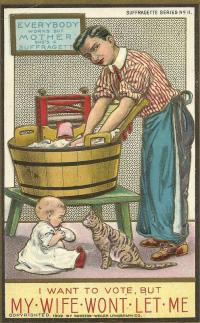 Image of a man wearing an apron doing the wash in a barrel while a small child plays at his feet